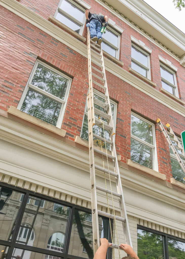 Upward photo of Superior Cleaning Systems using a ladder to clean upper floor commercial windows